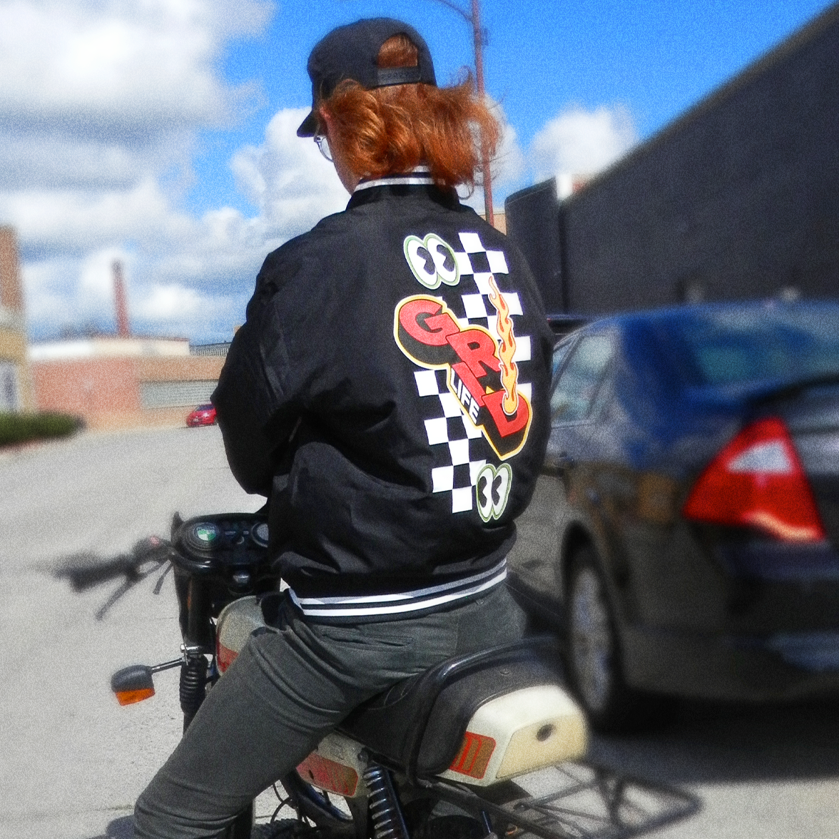 Back of the GRIDLIFE lightweight bomber jacket with rider on moped outside
